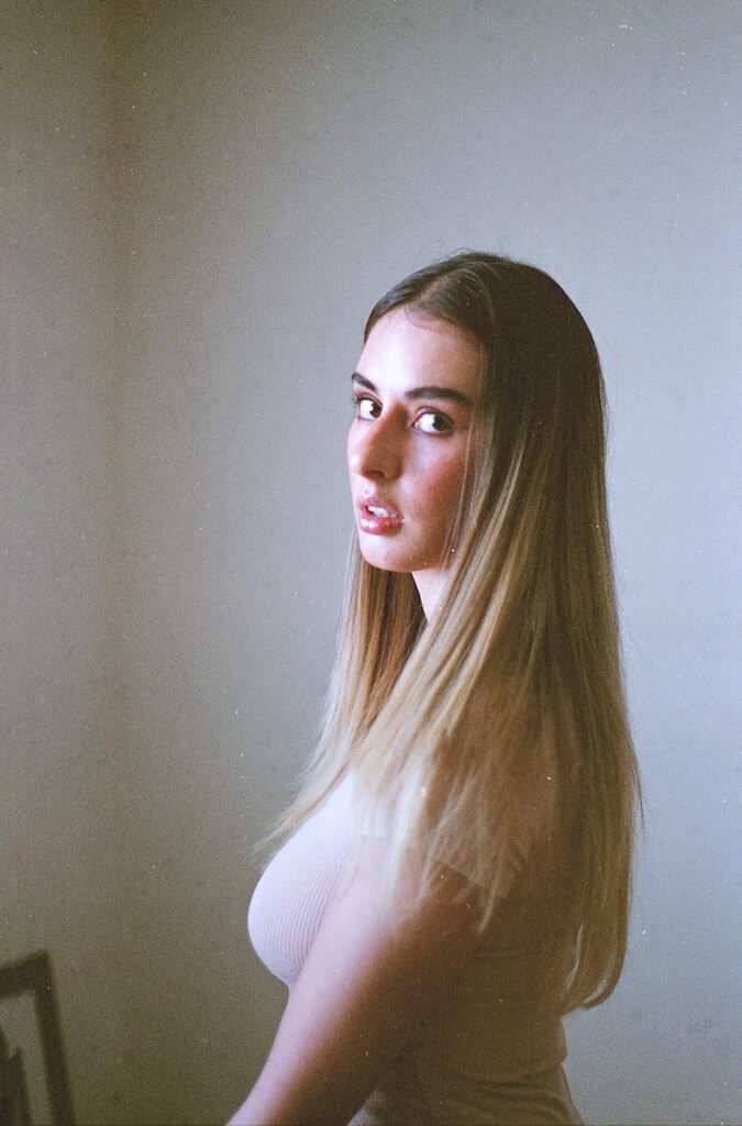 Film Photo of Marintia Bustos a model with long blonde hair looking over her shoulder with a side profile set against a softly lit background.